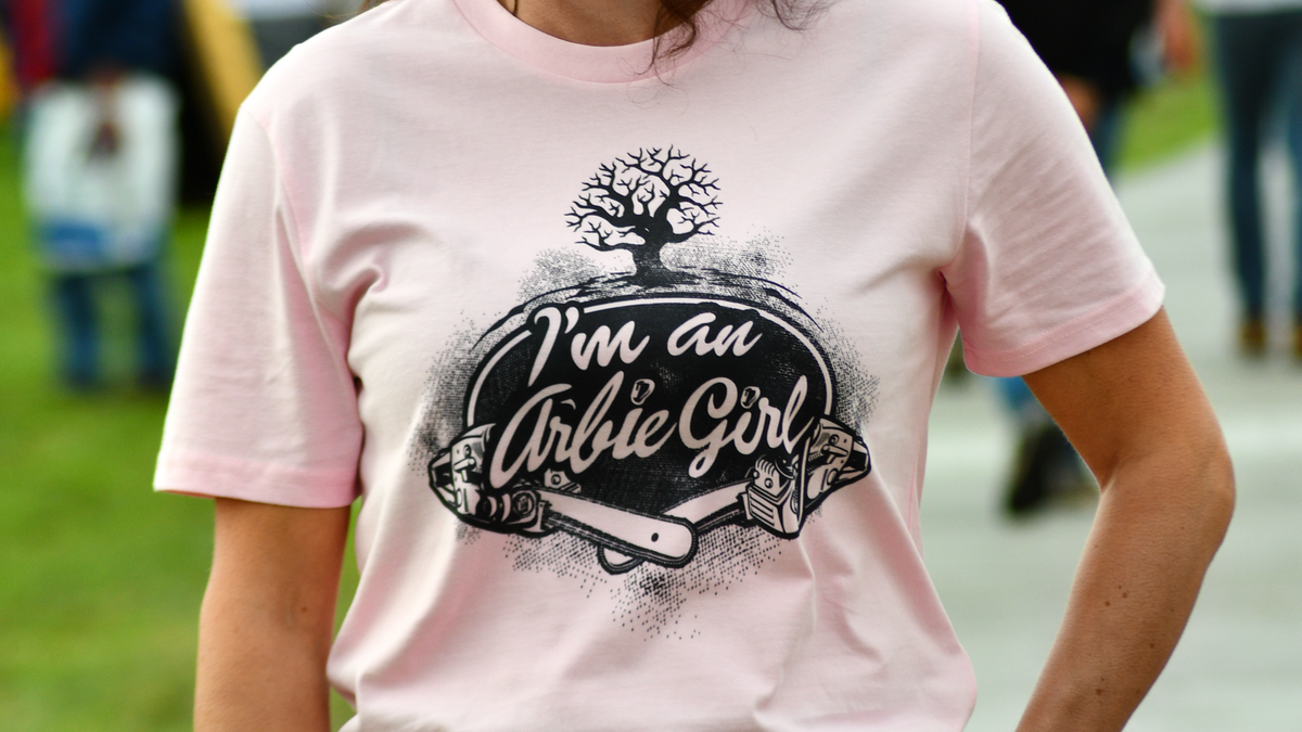 A woman wearing a light pink graphic t-shirt with the text 'I'm an Arctic Girl' and a tree illustration, standing outdoors at what appears to be an event or fair.